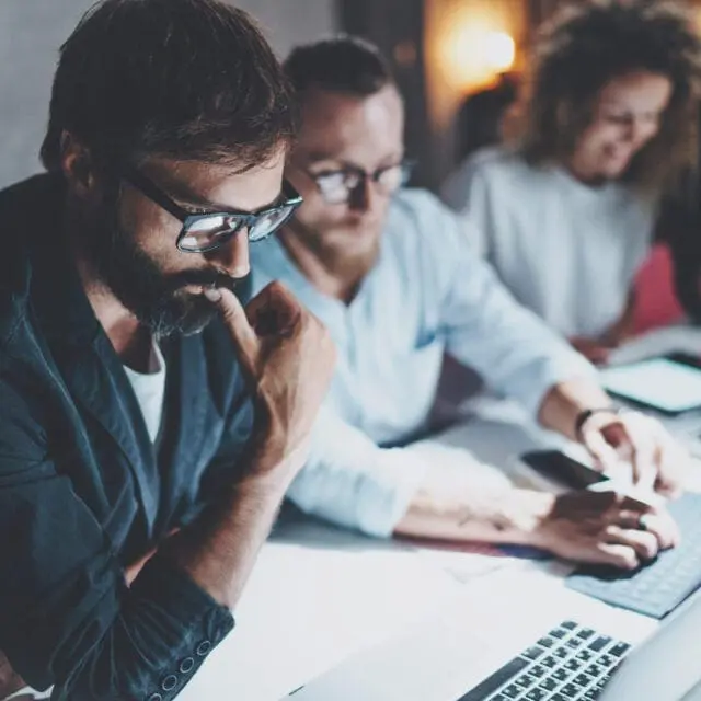 A man working in an office looks pensive, looking down with thumb on lips.