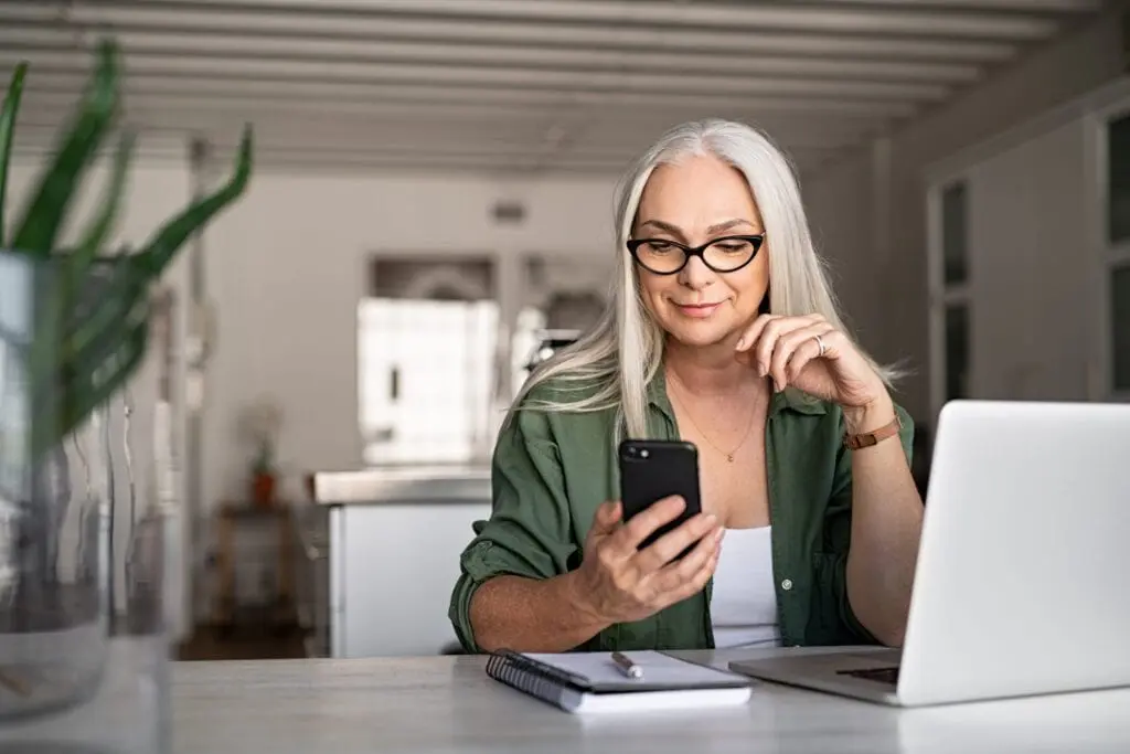 Digital identity for Canada: A woman sitting at a kitchen table works with a laptop and smartphone