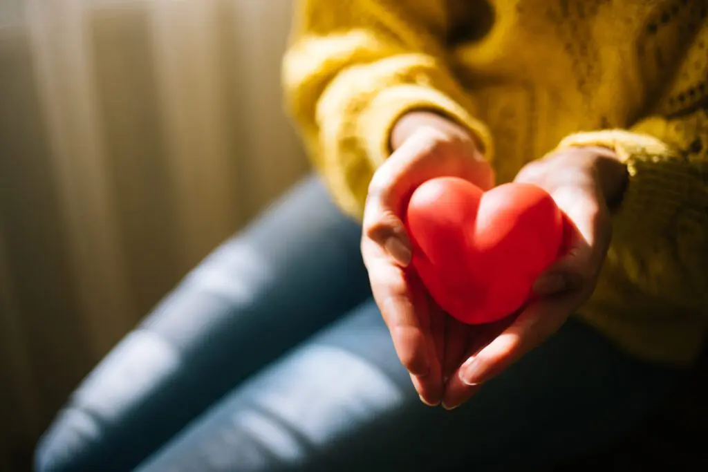 A woman holds a red toy heart in her hands.