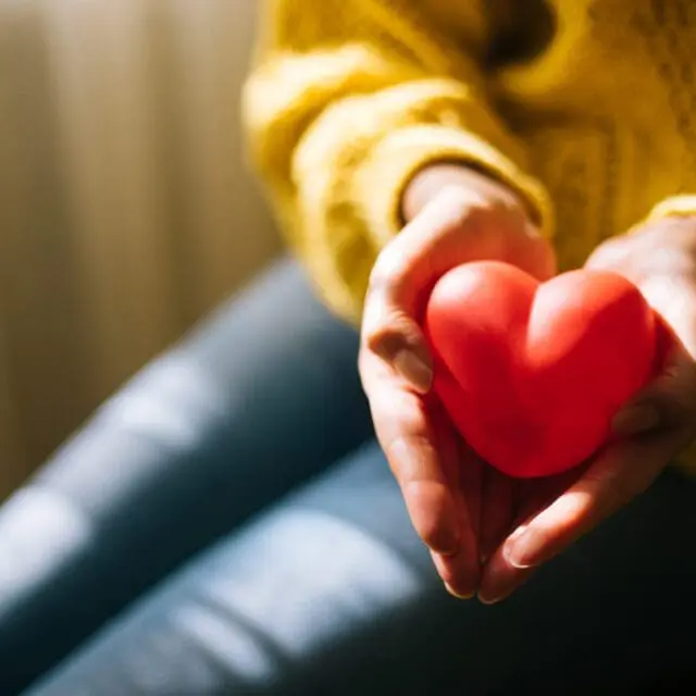 A woman holds a red toy heart in her hands.