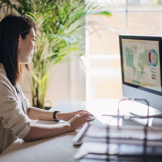 Woman works on desktop with world map on the screen, as digital currency creates a finance transformation.