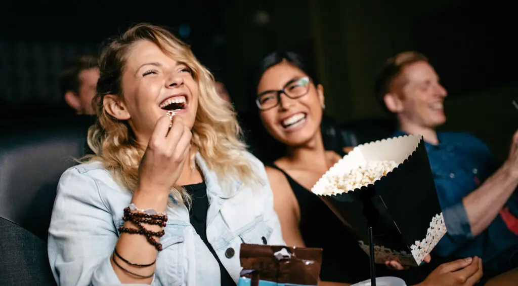 Friends enjoying popcorn and watching a movie at a cinema.