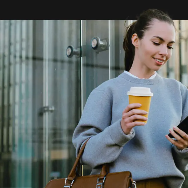 person holding coffee cup looking at phone