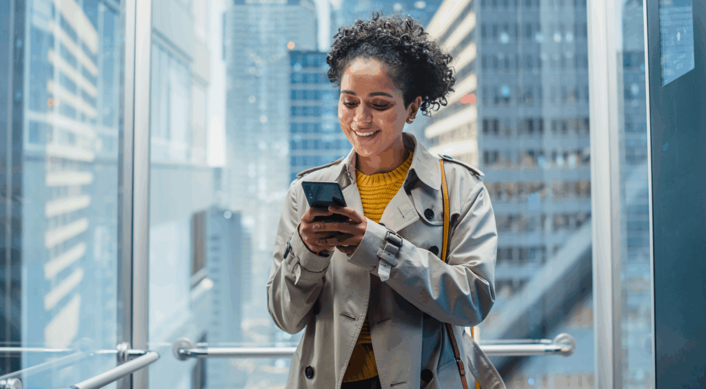 Une femme dans un ascenseur regarde son téléphone en souriant.