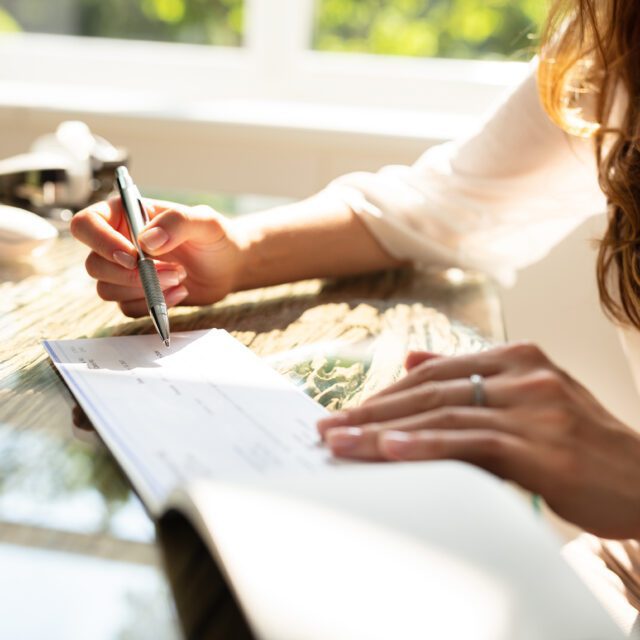 A desk is littered with receipts and other papers; a man’s hand works a calculator.