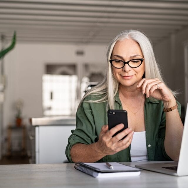 A smiling woman holds up a smartphone to look at screen.