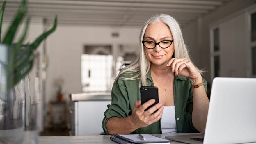 A smiling woman holds up a smartphone to look at screen.