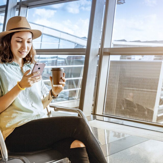 Digital ID in air travel: Smiling young woman in airport lounge looks at her phone