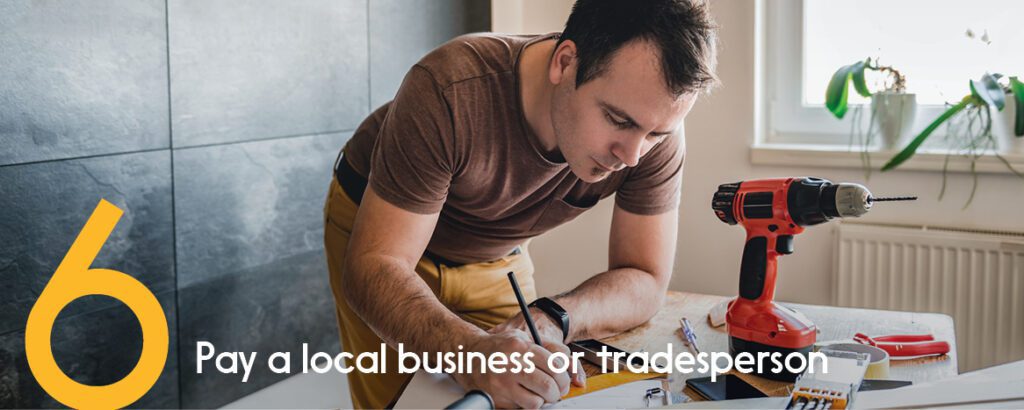 A tradesperson is standing over a desk surrounded by tools and looks over his renovation plans.