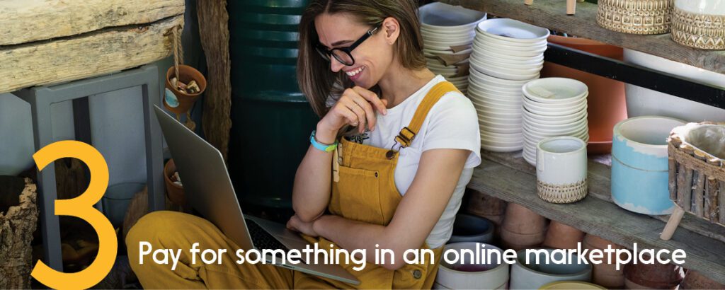 A smiling woman shopowner sits and looks over the digital transactions on her laptop.