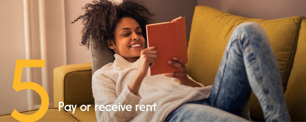Woman is relaxing with a book on her couch and smiling as her autodeposit goes through. 