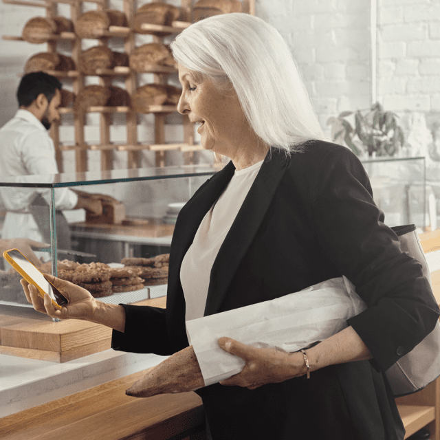 Une femme en tailleur dans un café regarde son cellulaire en souriant grâce aux paiements accélérés