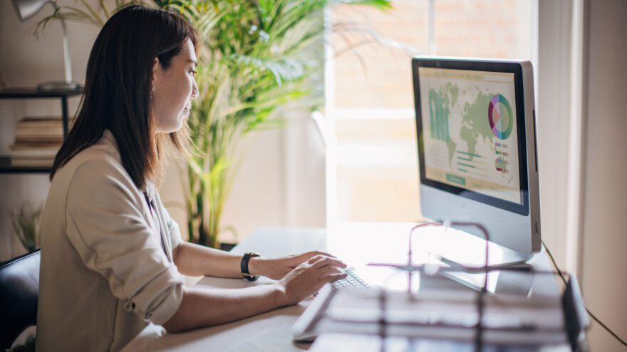 Woman works on desktop with world map on the screen, as digital currency creates a finance transformation.