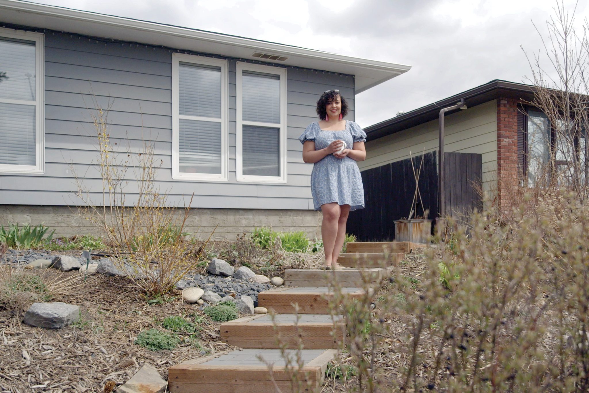 Heather stands on a hill in front of her house wearing a blue dress.