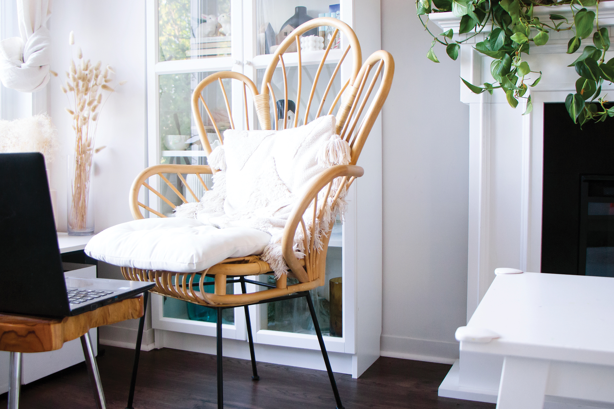 A brightly lit room shows a tall, elaborate wicker chair with a white pillow sitting in front of a laptop.