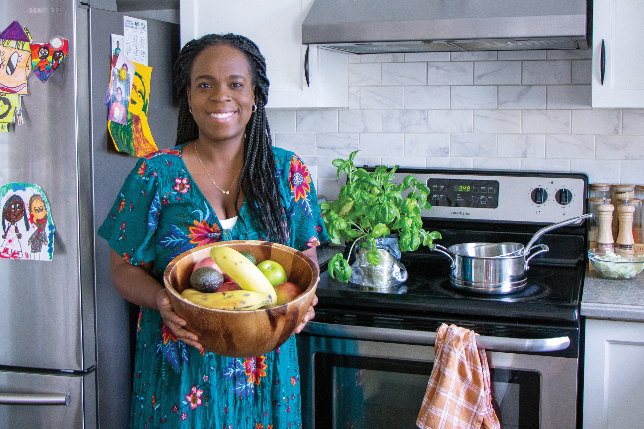 Marielle is smiling as she stands in a brightly lit kitchen holding a wooden bowl filled with colourful fruit.