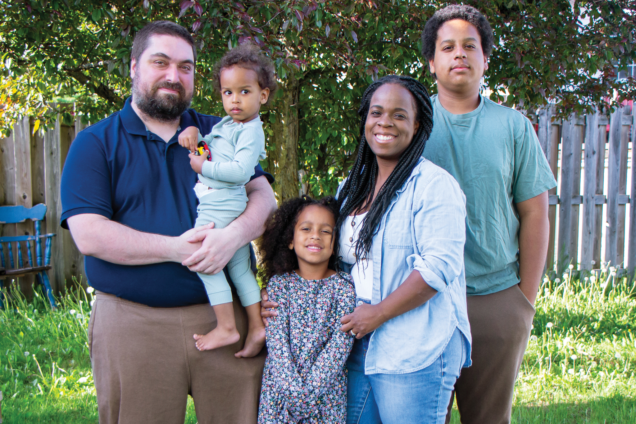 Marielle stands in a green backyard with her husband, surrounded by their three children.