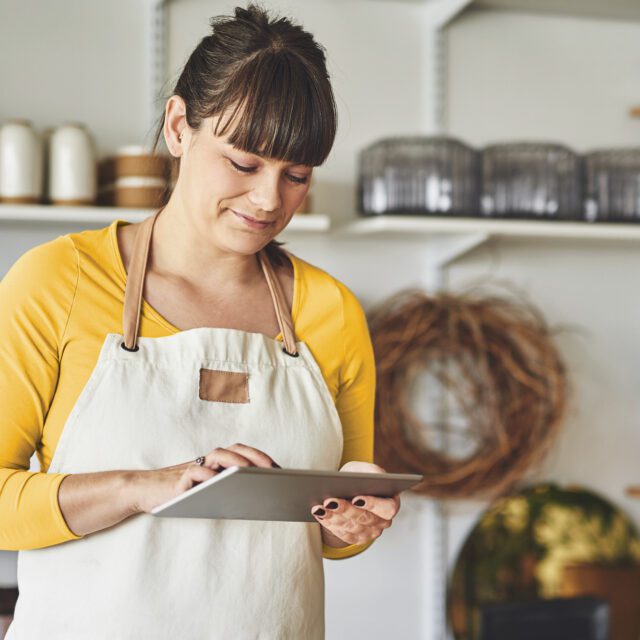 Woman running a small business smiles and makes an Interac e-Transfer transaction on her tablet.