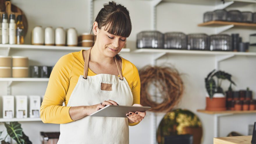 A woman wearing an apron in a café uses a tablet.