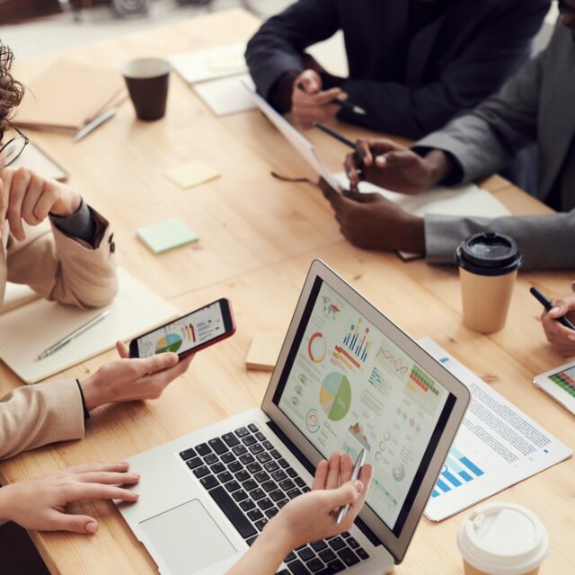 A group of people in work attire sit at a table working with digital devices.