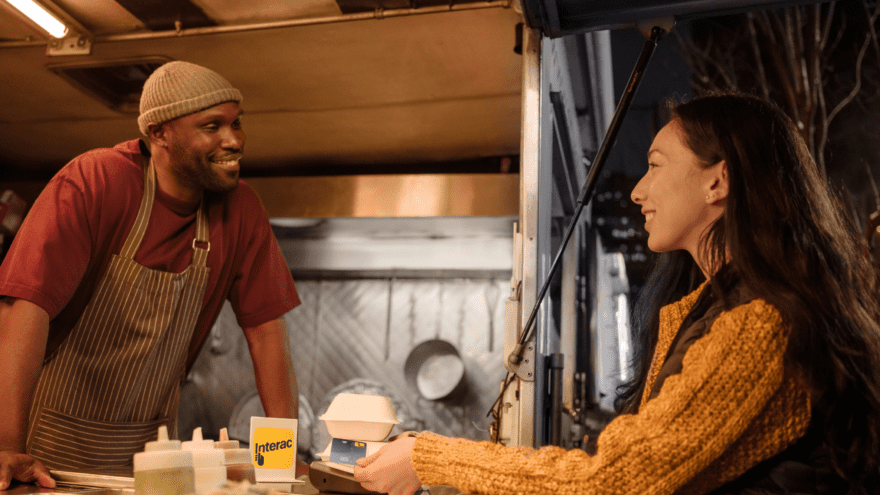 Woman in yellow sweater making INTERAC Debit transaction at a small business